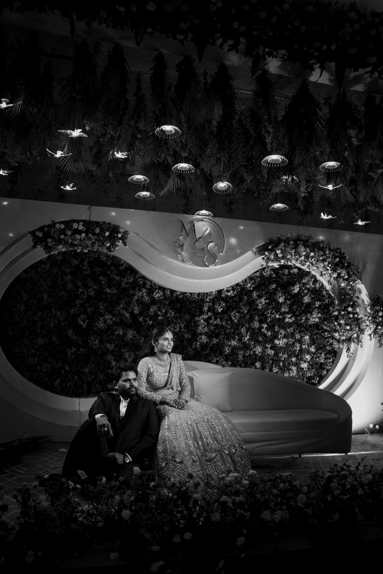 Sivakanth and Mridula seated together on a sofa beneath a canopy of hanging lights
